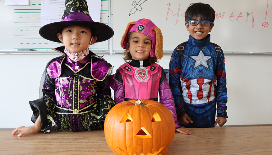 Three happy elementary students wearing Halloween costumes